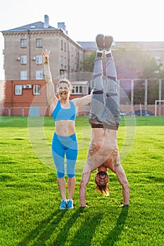 Man standing on his hands upside down and woman holding him. Strong, muscular extreme sportsmen. Young athletes of Caucasian