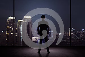 Man standing in his office looking at the city at night