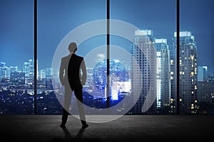 Man standing in his office looking at the city at night