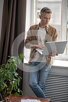 Man standing holding laptop looking at screen