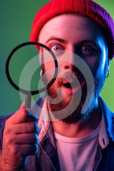 Man standing, holding magnifying glass and looking at camera, having astonished surprised face.