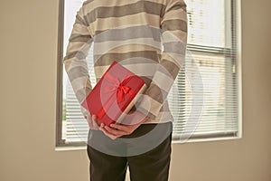 Man standing and holding red gift box behind his back