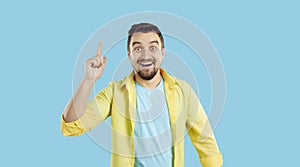 Man standing isolated on a blue background has an idea, smiles and points his finger up