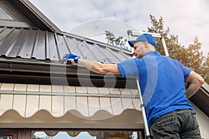 Man standing on ladder and cleaning roof rain gutter photo
