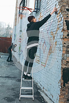 man standing on ladder and painting colorful graffiti