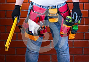 Man with standing level in his hand against the background of a red brick wall with a full tool bag. DIY