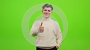 The man is standing and looking at the camera. He is pointing his finger up. He is standing on a green background. Green