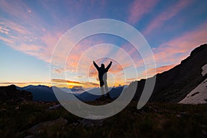 Man standing on mountain top outstretching arms, sunrise light colorful sky scenis landscape, conquering success leader concept.