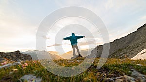 Man standing on mountain top outstretching arms, sunrise light colorful sky scenis landscape, conquering success leader concept.