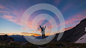 Man standing on mountain top raising arms, sunrise light colorful sky scenis landscape, conquering success leader concept.