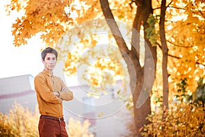 Man standing in a mustard shirt and brown trousers against the background of an autumn forest