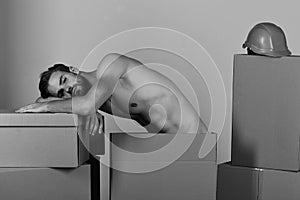 Man standing naked among cardboard boxes. Sexuality and building concept: guy with torso resting