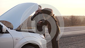 Man standing near broken car and calling for help on phone