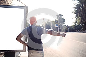 Man standing near bus stop thumbing a lift