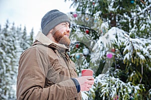 Man standing near decorated christmas tree and drinking coffee outdoors