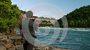 Man standing near a river, capturing photographs with a digital camera