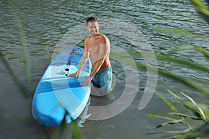 Man standing near SUP board in river water on sunny day