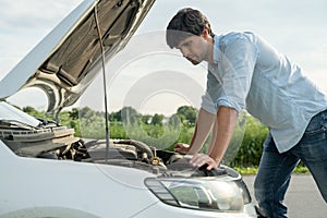 Man standing next to a broke down car, looking down at engine in frustration