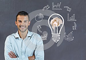 Man standing next to light bulb with crumpled paper ball and business graphics in front of blackboa