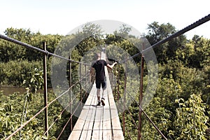 A man standing on the old broken wooden bridge. Bridge above the river aming the green forest. Summer walking