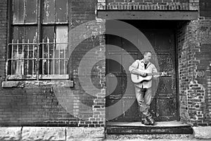 Man standing on old factory building loading dock playing acoustic guitar