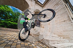 man standing on one wheel of a mountain bike. Horizontal shot outdoors in the city with architecture in the background