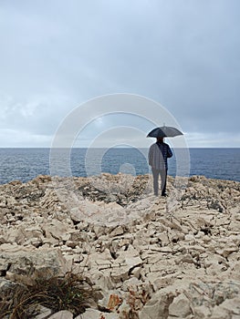 Man standing outdoors close the sea with umbrella on rainy day