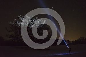 Man standing outdoors at night in Sweden Scandinavia winter landscape shining with flashlight at tree and sky