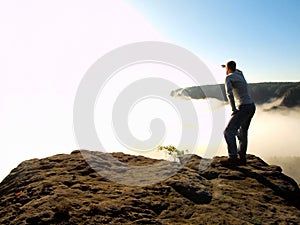 Man is standing on the peak of sandstone rock in national park Saxony Switzerland and watching over the morning misty valley