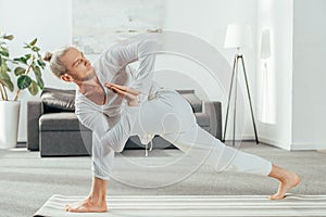man standing in Revolved Side Angle exercise, Parivrtta Parsvakonasana pose on yoga mat