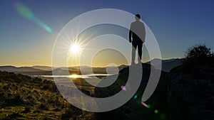 Man standing on a rock with his back facing the sunset over the mountains. Navacerrada Madrid