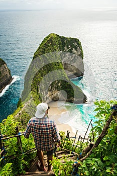 Man standing on a rock ladder at the edge of a cliff on Nusa Penida island