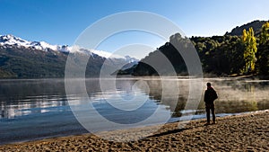 Man standing on the shores of an evaporating lake with a snowy mountain range in the background. Gutierrez Lake, Los Alerces