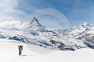 A man standing on the snow in the background of Matterhorn.