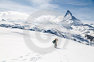 A man standing on the snow looking at the background of Matterhorn.