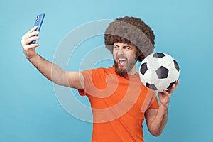 Man standing with soccer ball and broadcasting livestream from football match.