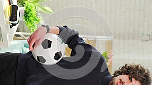 Man standing with soccer ball in front of the camera on bright room background.