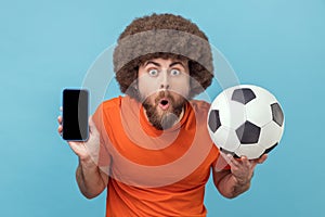 Man standing with soccer ball and showing cell phone with empty display for advertisement.