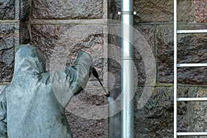 Man standing on a stepladder washes the walls of the building with a jet of water under pressure. Chemical protective suit.