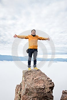 Man standing on a stone with his arms wide open on top of a mountain