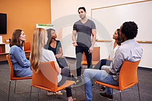 Man Standing To Address Group Of Men And Women At Mental Health Group Therapy Meeting