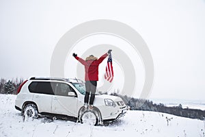 man standing on the top of the hill with usa flag in his hands near suv car looking for beautiful winter view