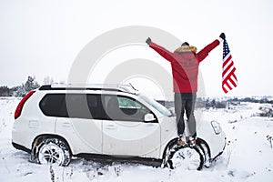 man standing on the top of the hill with usa flag in his hands near suv car looking for beautiful winter view