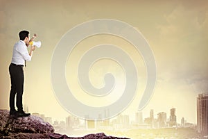 Man standing on the top of mountain, yelling using megaphone