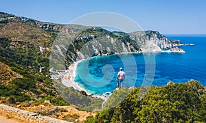 Man standing on top of a rock with an exciting feeling of freedom, looking at Petani Beach. Kefalonia ionian island