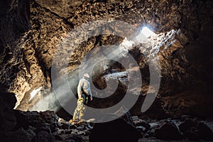 Man standing under the light in the mountain cave. Extreme adventure travel concep