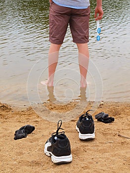 Man standing in water with shoes on the sand.