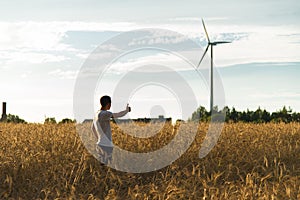 A man standing in a field looking at a wind generator
