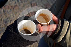 Man standing with woman and drinking quality espresso in winter in the square. They drink from a brown paper cup. The man has glov