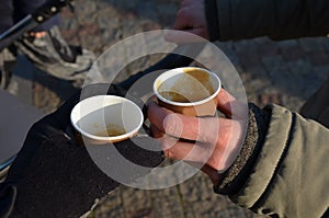 Man standing with woman and drinking quality espresso in winter in the square. They drink from a brown paper cup. The man has glov